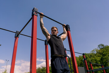 Fototapeta premium portrait of a young sweaty sportsman doing horizontal bar swings arms and shoulders push-ups on the sports ground during street training
