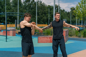 Personal fitness trainer training athlete on sports ground Two active guys training outdoors doing warm-up before exercise