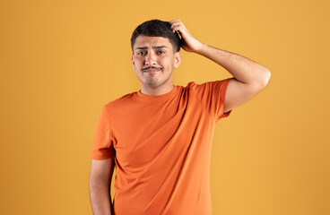 Fototapeta na wymiar Sad pensive brazilian guy thinking and scratching head, posing isolated on orange background, studio shot