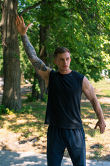 portrait of a young sportsman with tattoos doing warm-up exercises outdoors street training in the park motivation