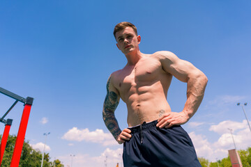 young sportsman bodybuilder standing on sports field outdoor workout beautiful sexy pumped body abs...