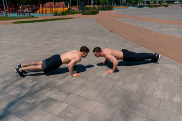 trainer and young sportsman doing push-ups on the street and giving each other a high five during...