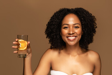 Cheerful pretty young black woman drinking water with orange © Prostock-studio