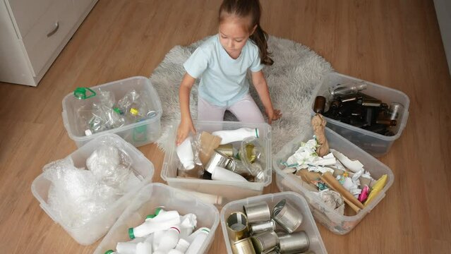 Toddler girl sorting recyclable items at home. Toddler sort collected plastic, paper, glass, stretch film, and cans for recycling to baskets. Concept of education of responsible consumption.