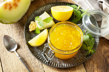 Homemade preserve. Sweet melon and citrus jam or jelly in small glass jar with fresh melon slices on wooden rustic table.