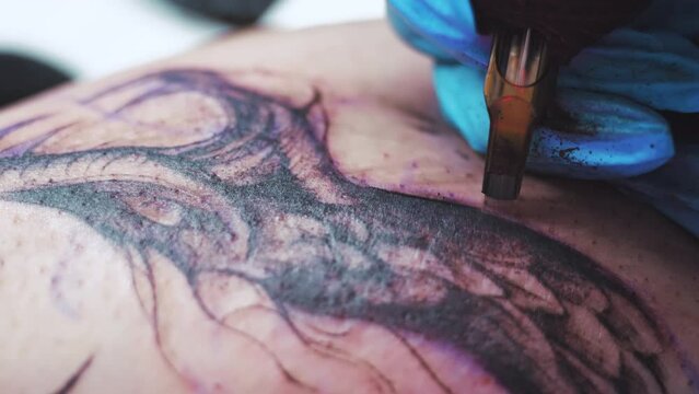 Professional tattoo master makes tattoo using tattoo machine in tattooing studio. High quality 4k footage