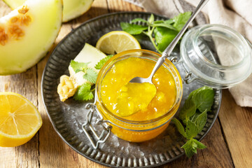 Sweet melon and citrus jam or jelly in small glass jar with fresh melon slices on wooden rustic table. Homemade preserve.