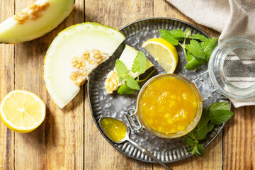 Sweet melon and citrus jam or jelly in small glass jar with fresh melon slices on wooden rustic table. Homemade preserve. View from above.