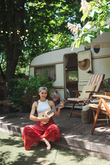 Happy hippie girl are having a good time with playing on guitar in camper trailer. Holiday, vacation, trip concept.
