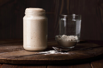 Sourdough bread starter with bubbles with white flour on dark wooden rustic background, fermentation, natural homemade baking and cuisine concept