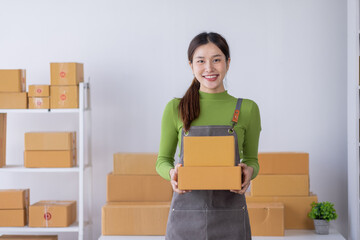 Startup happy Asian woman business owner works with a box at home, prepare parcel delivery SME supply chain, procurement, package box to deliver to customers, Online SME business entrepreneurs ideas,
