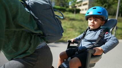 Fototapeta na wymiar Child in the back seat of bicycle riding with mother kid in bike back seat wearing helmet