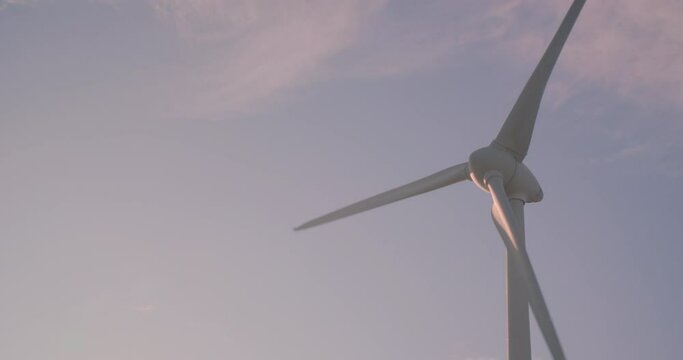 Wind turbine windmill turning in a blue sky with pink clouds
