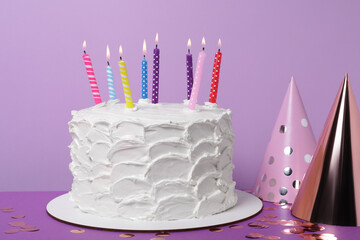 Delicious cake with burning candles and festive decor on purple background