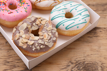 Obraz na płótnie Canvas Box with different tasty glazed donuts on wooden table, closeup