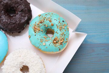 Box with different tasty glazed donuts on light blue wooden table, closeup