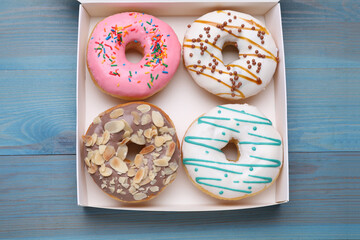 Box with different tasty glazed donuts on light blue wooden table, top view