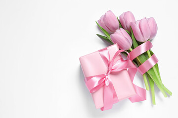 Beautiful gift box with pink bow and tulips on white background, flat lay. Space for text
