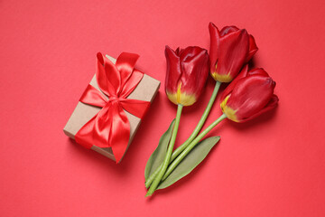 Beautiful gift box and tulips on red background, flat lay