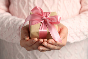 Woman holding gift box with pink bow, closeup