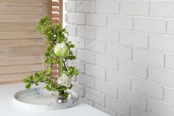 Beautiful ikebana for stylish house decor. Floral composition with fresh tulip flower and blooming branches on white table, space for text