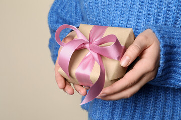 Woman holding gift box with pink bow on beige background, closeup. Space for text