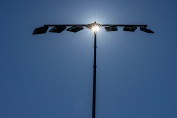 Sports field lights silhouetted against sun
