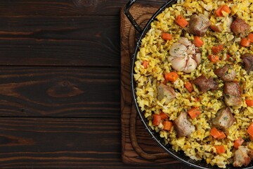 Delicious pilaf with meat, carrot and garlic on wooden table, top view. Space for text
