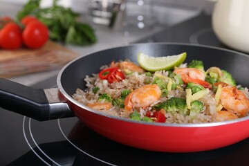 Tasty rice with shrimps and vegetables in frying pan on induction stove, closeup