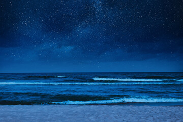 Sea waves rolling onto sandy beach under starry sky at night