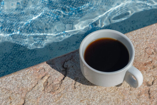 Cup of coffee on the poolside of the swimming pool.

