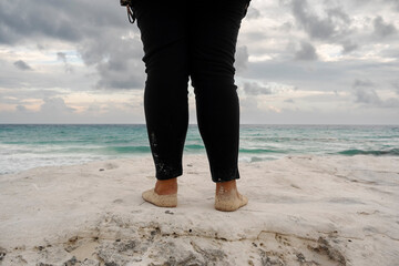 Close up back angle of an anonymous person's feet full of sand and standing in front of the sea