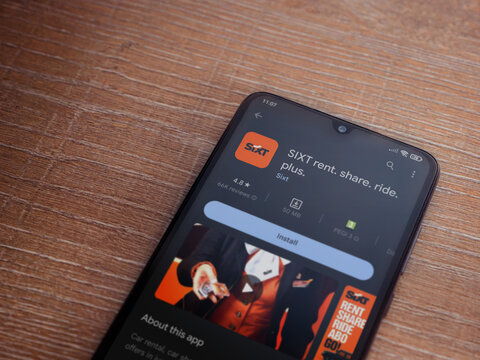 Lod, Israel - July 16,2023: SIXT rent app play store page on smartphone on wooden background. Top view flat lay with copy space.