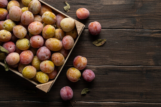 Plums in a wooden box, on wooden table.