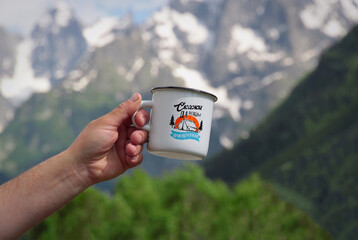The traveler holds a cup of coffee in the mountains. White mug in the hands on the background of the mountains. Mountain camping concept.