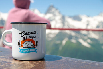 A white mug of hot tea on a wooden table against the backdrop of a snowy mountain range. Text - Say yes to new adventures