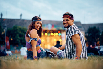 Happy couple relaxing on grass in front of stage during summer music festival.