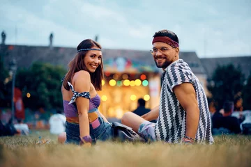 Fototapeten Happy couple relaxing on grass in front of stage during summer music festival. © Drazen