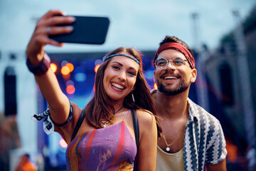 Happy couple taking selfie in front of stage during summer music concert.