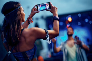 Young woman photographing her boyfriend with cell phone at summer music festival.