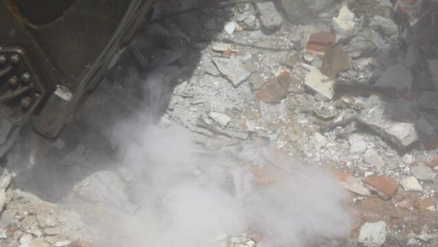 Excavator scraping the ground of demolition site. Close up. Breaking up the concrete footings. Digger turns old home into rubble and dust fills the air. Concrete dust released by a building demolition