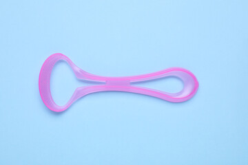 Pink tongue cleaner on light blue background, top view