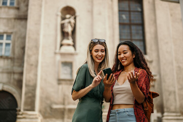 Smiling young females using a phone while walking through a city street while on vacation