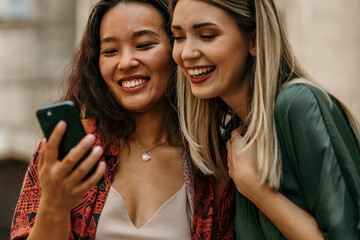 Young diverse female friends using a cellphone while walking through a city street while on vacation