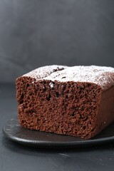 Tasty chocolate sponge cake with powdered sugar on black table, closeup