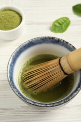 Cup of fresh matcha tea with bamboo whisk on white wooden table, above view