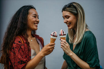 Two multiracial happy women having conversations and eating ice cream outdoors - Friendship and summer vacation concept