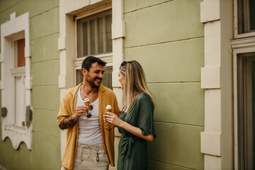 Tourists stroll hand-in-hand along a charming city street, with ice cream cones in the other hand, savoring the flavors and sights.