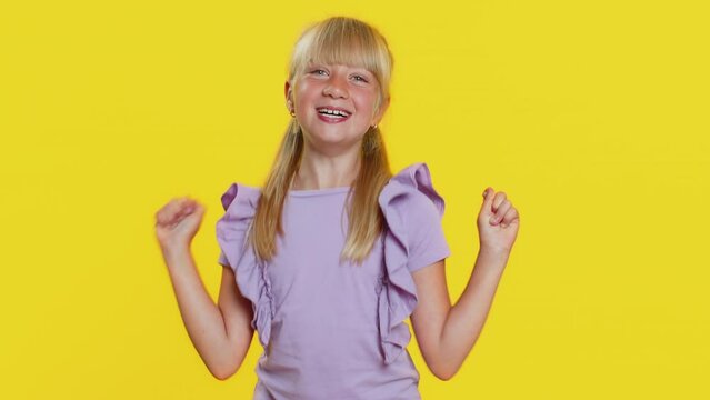 Young preteen child girl kid shouting, raising fists in gesture I did it, celebrating success, winning, birthday, lottery jackpot goal achievemen. Little cute children isolated on yellow background