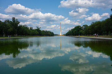 Washington Monument in Washington DC with across from the reflecting pond. Pictures taken  on a sunny summer day with a nice amount of clouds evenly spread out in the sky.